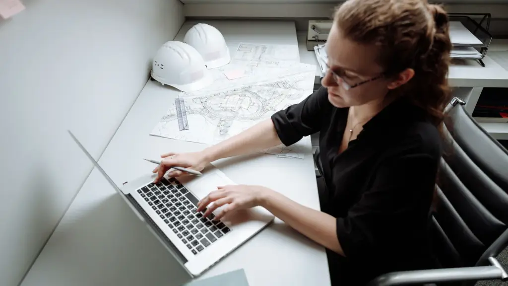 Architecte qui consulte le site internet de son agence sur un ordinateur portable, entourée de plans