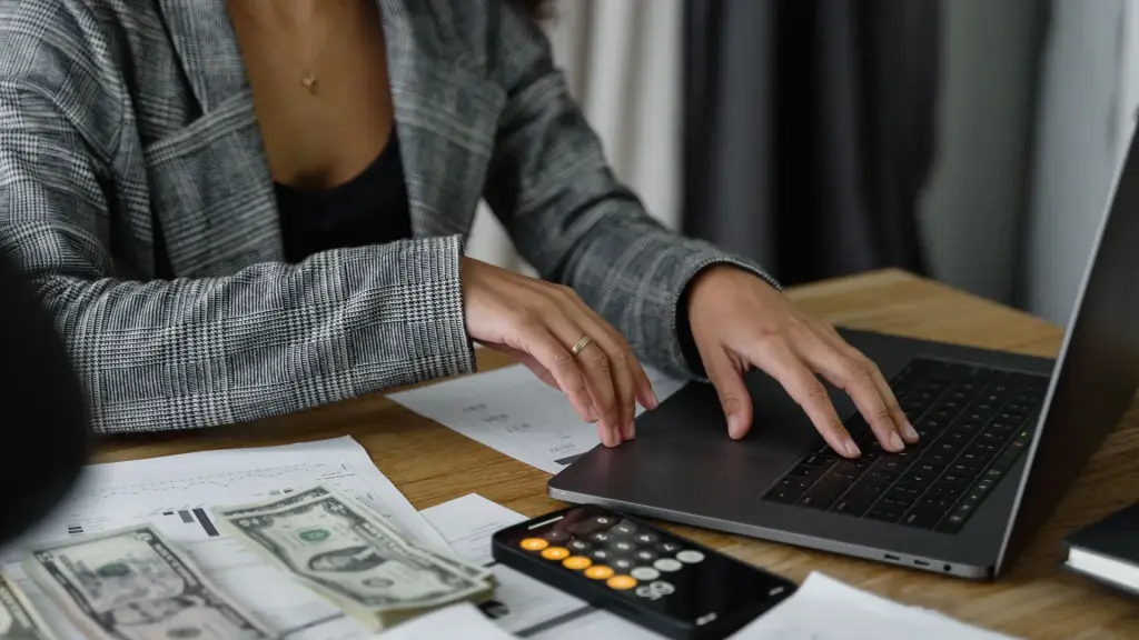 Mains sur le clavier d'un ordinateur portable, billets et calculatrice posés sur le bureau