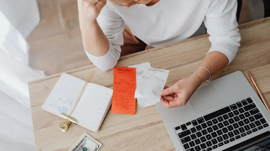 Personne qui lit un reçu devant son ordinateur portable, carnet ouvert sur la table