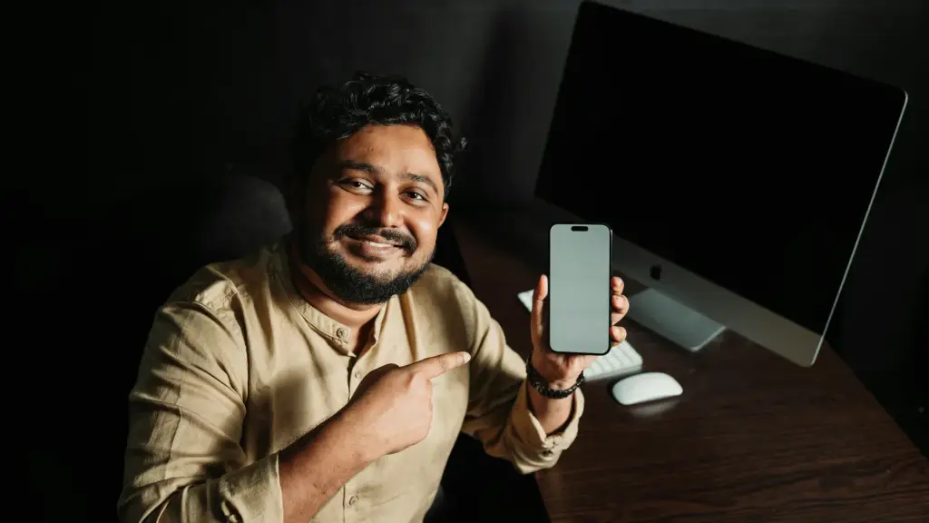 Homme souriant qui montre l'écran de son smartphone depuis son bureau